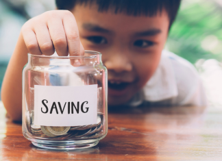 child putting coin in jar that says "saving" -tips for raising financially literate kids