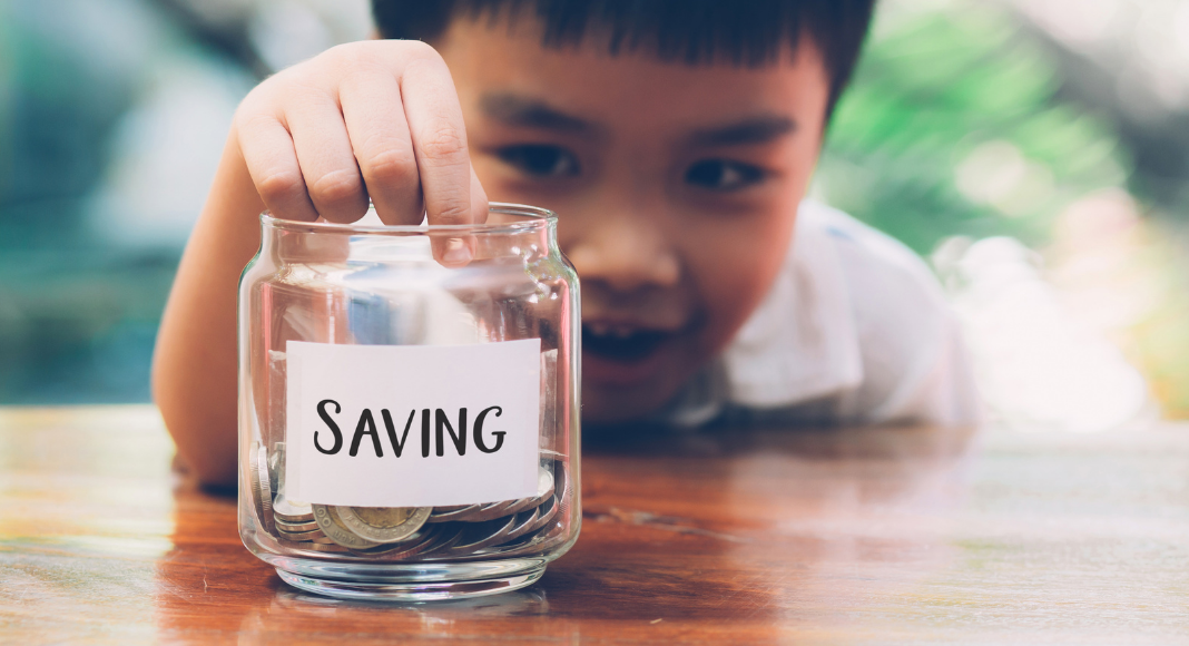 child putting coin in jar that says "saving" -tips for raising financially literate kids