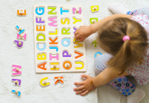 child playing on floor with wooden letter puzzle