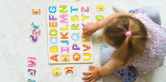 child playing on floor with wooden letter puzzle