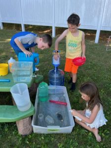 Two boys and a girl play with water toys from your recycling bin