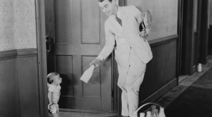 A man in a white delivery suit hands a milk bottle to a small child