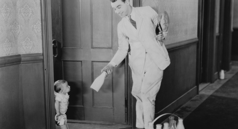 A man in a white delivery suit hands a milk bottle to a small child