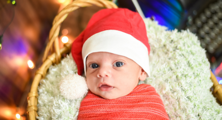 Newborn baby, swaddled, wearing a Santa hat in a basket