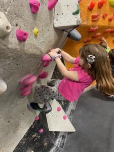 little girl holds on tight to rock climbing wall